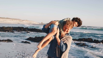 Père sur la plage qui porte son enfant et s'amuse avec lui