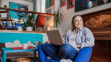 jeune femme avec un pc portable sur les genoux, assise dans un canapé