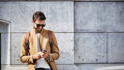 Homme souriant dans la rue, tenant son smartphone