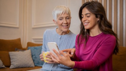 Femme âgée et sa petite fille sur un canapé, regardant un smartphone