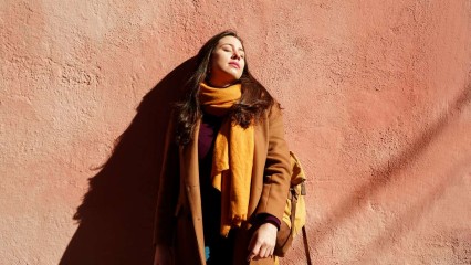 Femme appuyée contre un mur, au soleil, avec le sourire