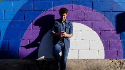 Un homme, portable à la main, appuyé contre un mur coloré