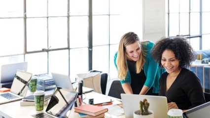 Deux femmes dans un bureau, face à un PC, avec le sourire