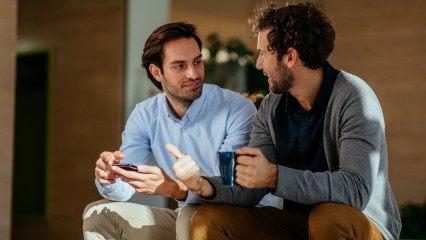 Deux hommes assis, qui discutent, un café à la main