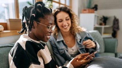 Deux femmes dans un canapé, qui regardent un smartphone avec le sourire