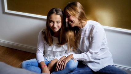Une femme et sa fille, assises par terre, complices et avec le sourire
