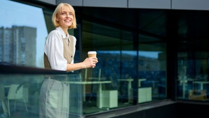 Femme sur un balcon de verre, un café à la main
