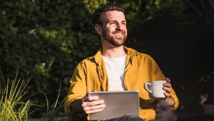 Homme assis en extérieur avec un café et une tablette en main