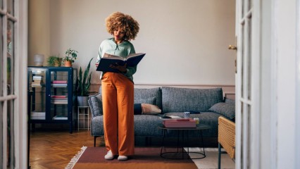 Femme debout dans son salon, en train de lire un énorme livre