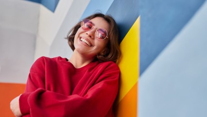Jeune femme appuyée contre un mur coloré, très souriante