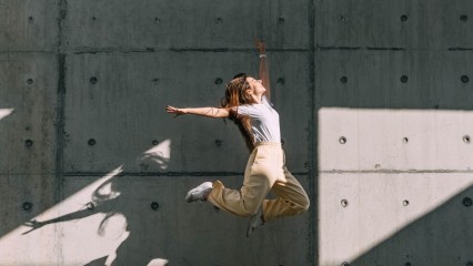 Femme qui saute devant un mur d'immeuble, face au soleil