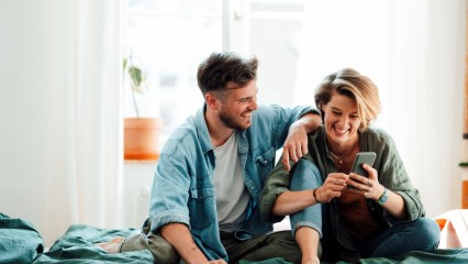 Un couple assis sur un lit, en train de discuter et de rire