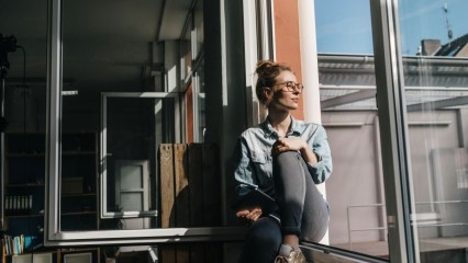 Femme qui regarde au loin, en étant assise sur le rebord d'une fenêtre