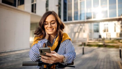 Femme en trotinette, à l'arrêt, tenant son téléphone