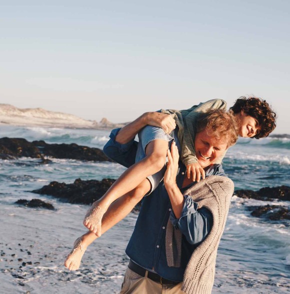Père sur la plage qui porte son enfant et s'amuse avec lui